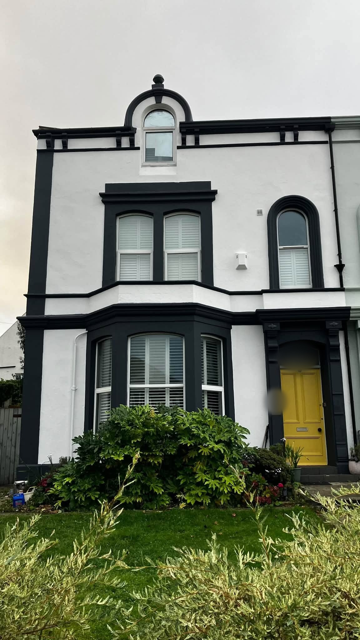 The same Victorian house front finished in white with black trim and a yellow front door
