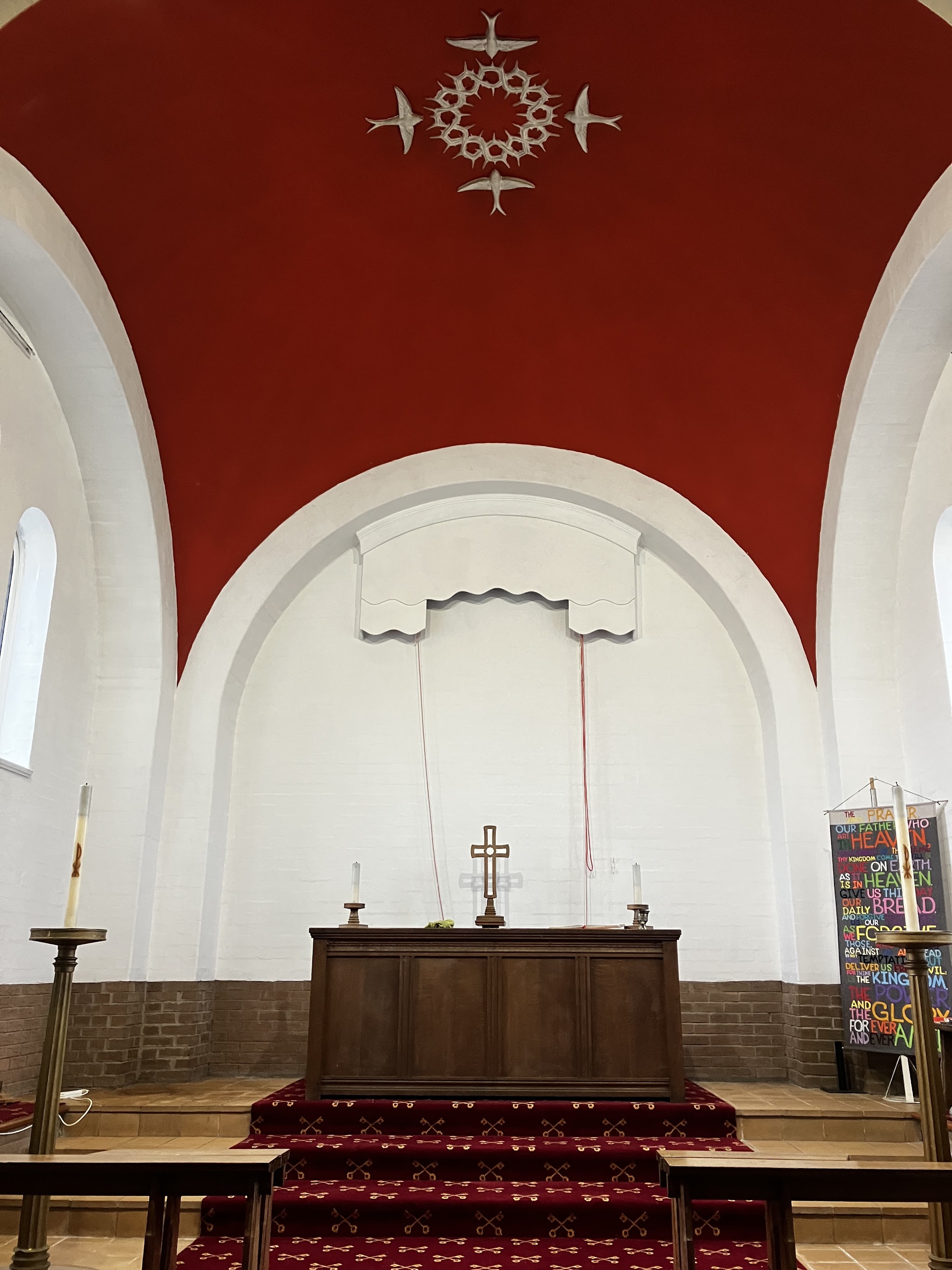 Church interior with a red vaulted ceiling over white arches and the altar